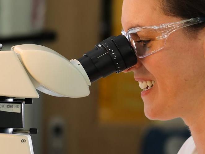Woman with safety goggles on looking through a biology microscope